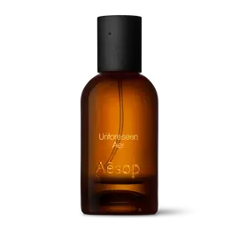 Bernsteinfarbene Flasche des Aesop Unforeseen Aer Eau de Parfum aus Glas mit schwarzem Verschluss vor weißem Hintergrund.