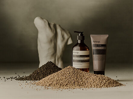 Aesop Antithesis Intense Body Cleanser pump bottle and tube beside piles of black peppercorns and coriander seeds.