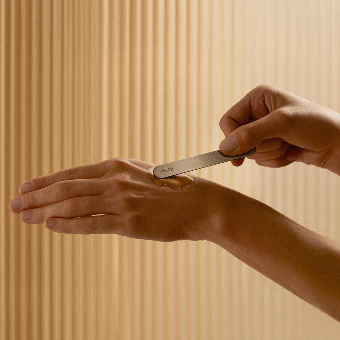 Une personne utilise une spatule Aesop pour appliquer un soin sur le dos de sa main.