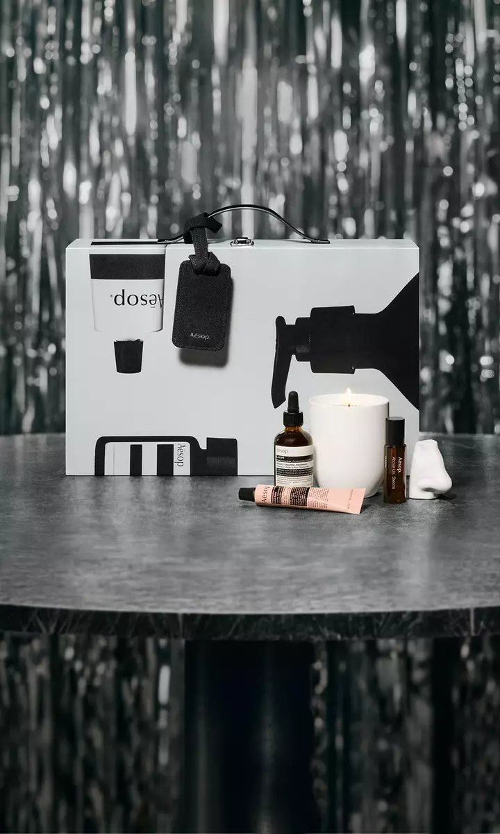 Aesop gift set and skincare products arranged on a table against a festive, softly lit backdrop.