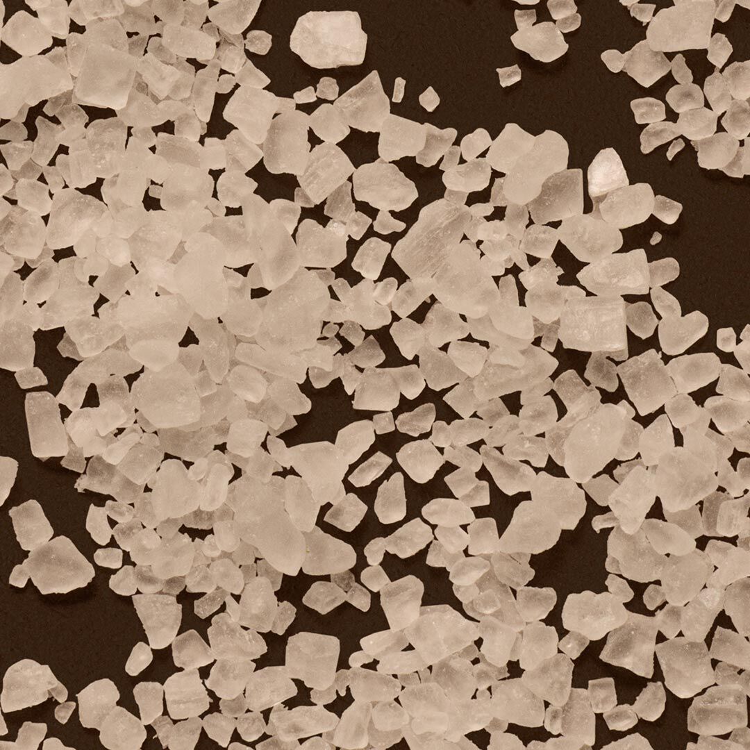 Close-up of coarse white salt crystals scattered across a dark surface.