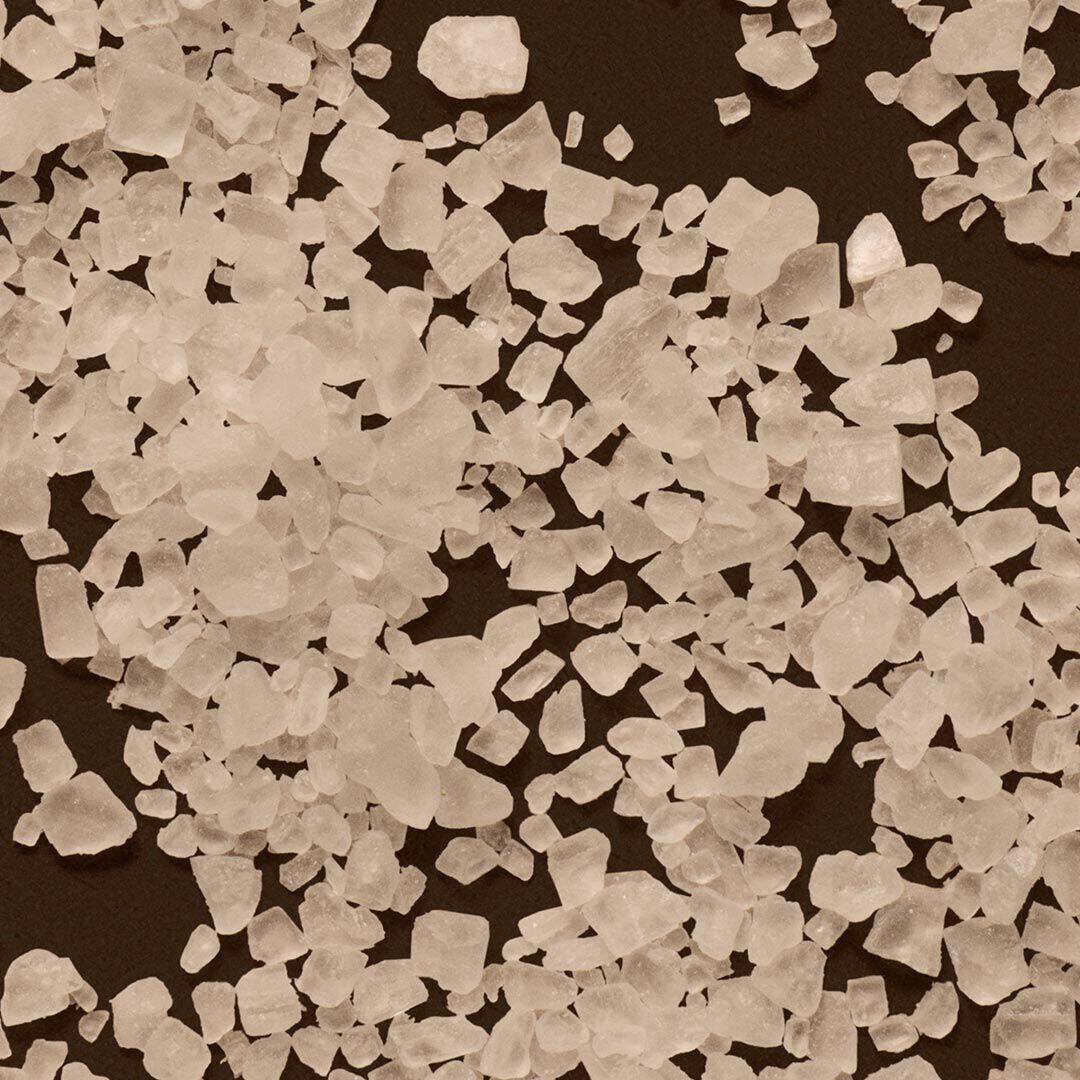 Close-up of coarse white salt crystals scattered across a dark surface.