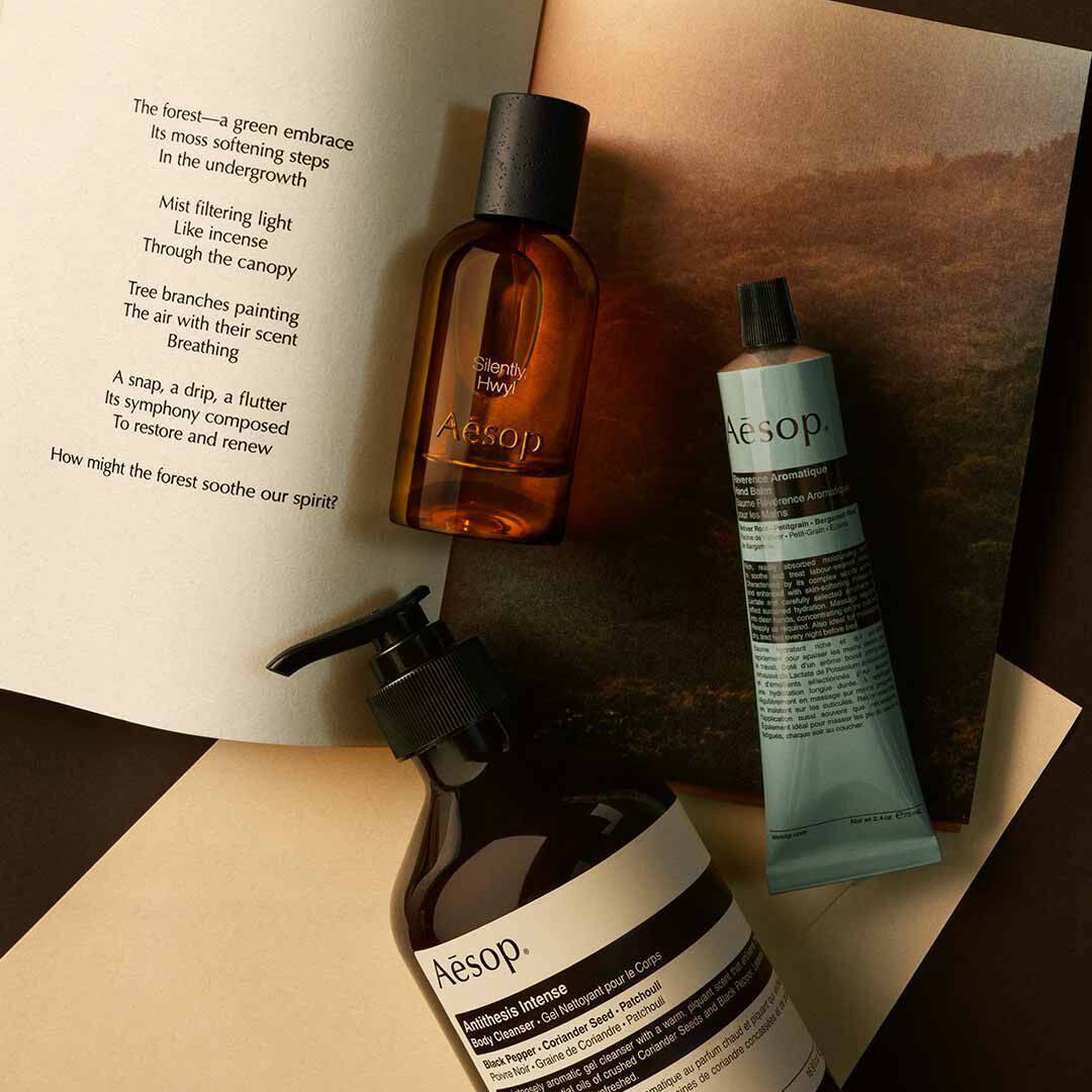 Flacon Aesop Silently Hwyl avec flacon-pompe et tube bleu, disposes sur des papiers avec une image de paysage.