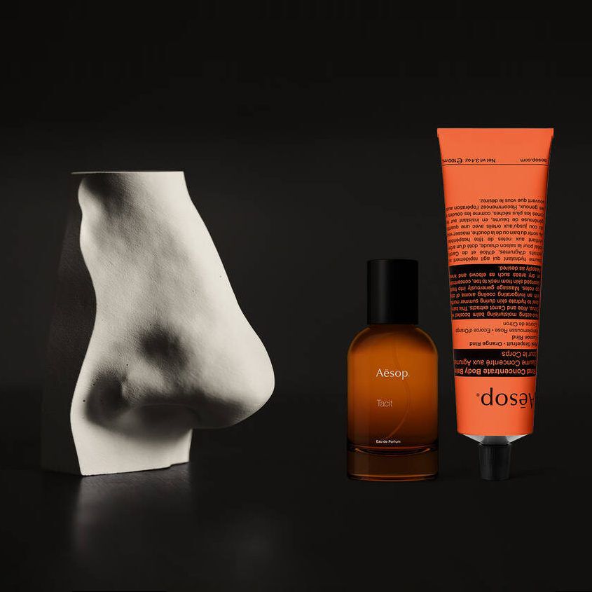 Flacon de parfum ambre et creme pour les mains corail a cote d’une sculpture blanche