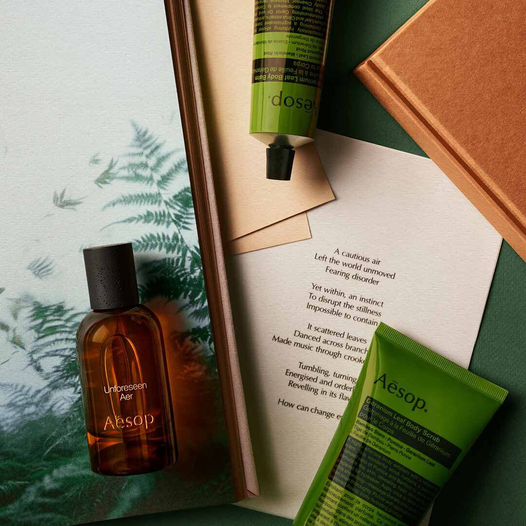 Aesop Unforeseen Aer Flakon mit Pumpspender und grunem Schlauch, arrangiert auf Papieren mit Farnmotiven.