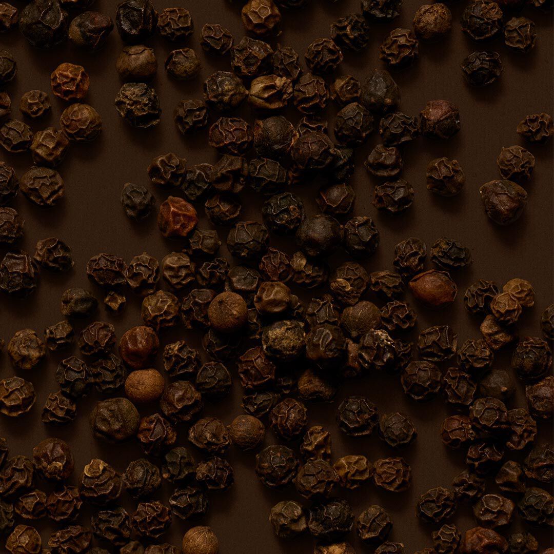 Close-up of peppercorns scattered across a dark brown surface.