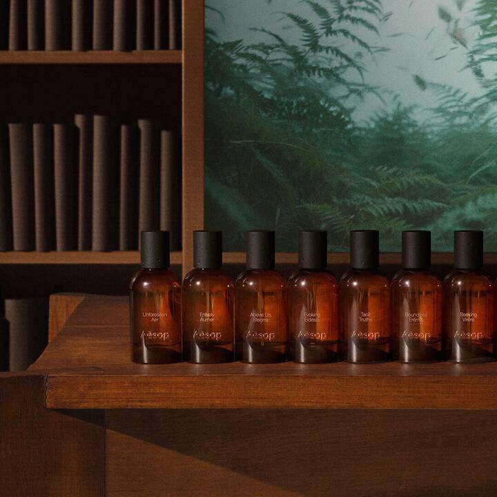 Eine Reihe von Aesop Parfumflaschen aus Bernsteinglas auf einem Holzregal.