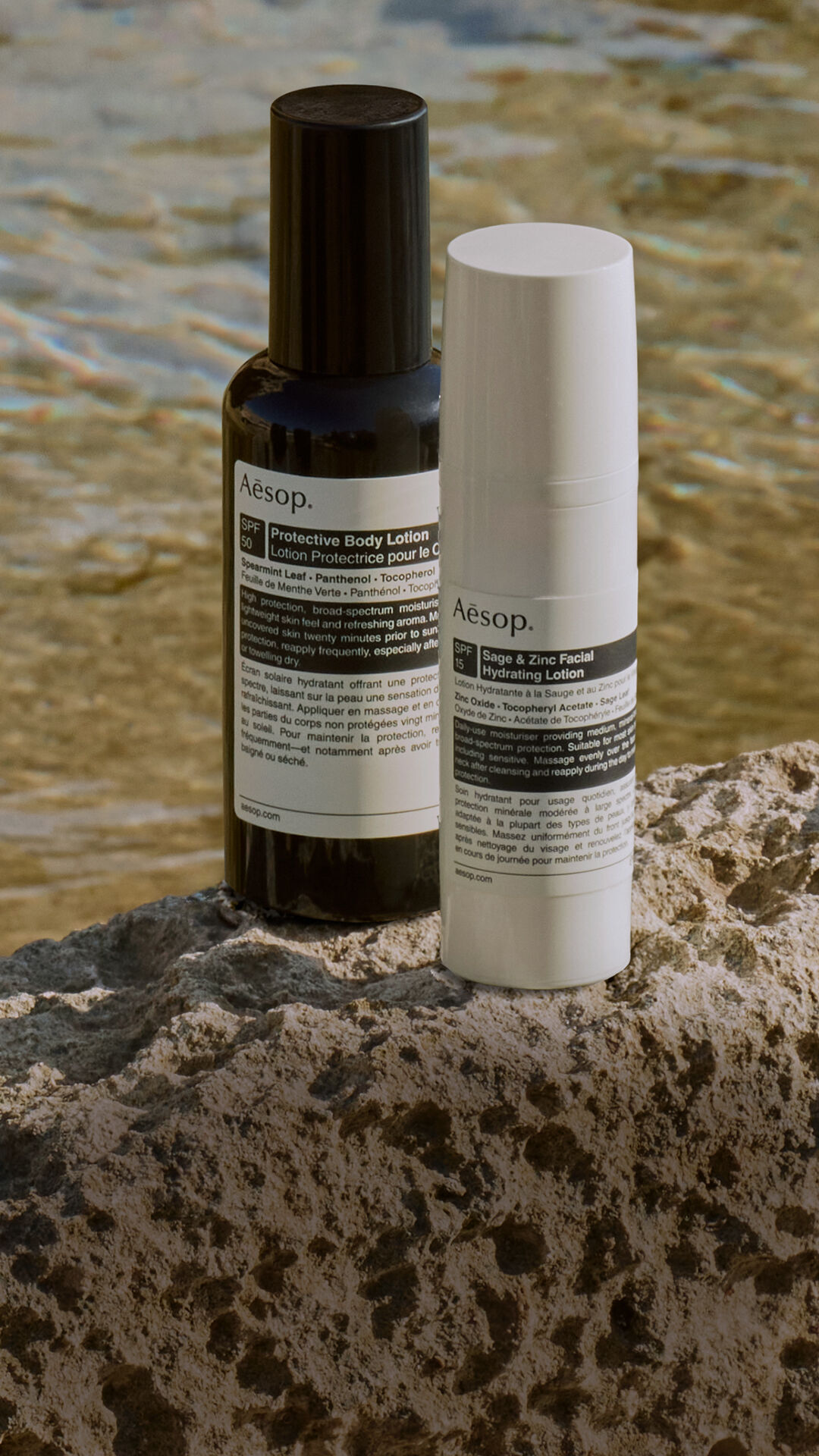 A curated selection of Aesop sun protection formulations resting on a rock by the sea.