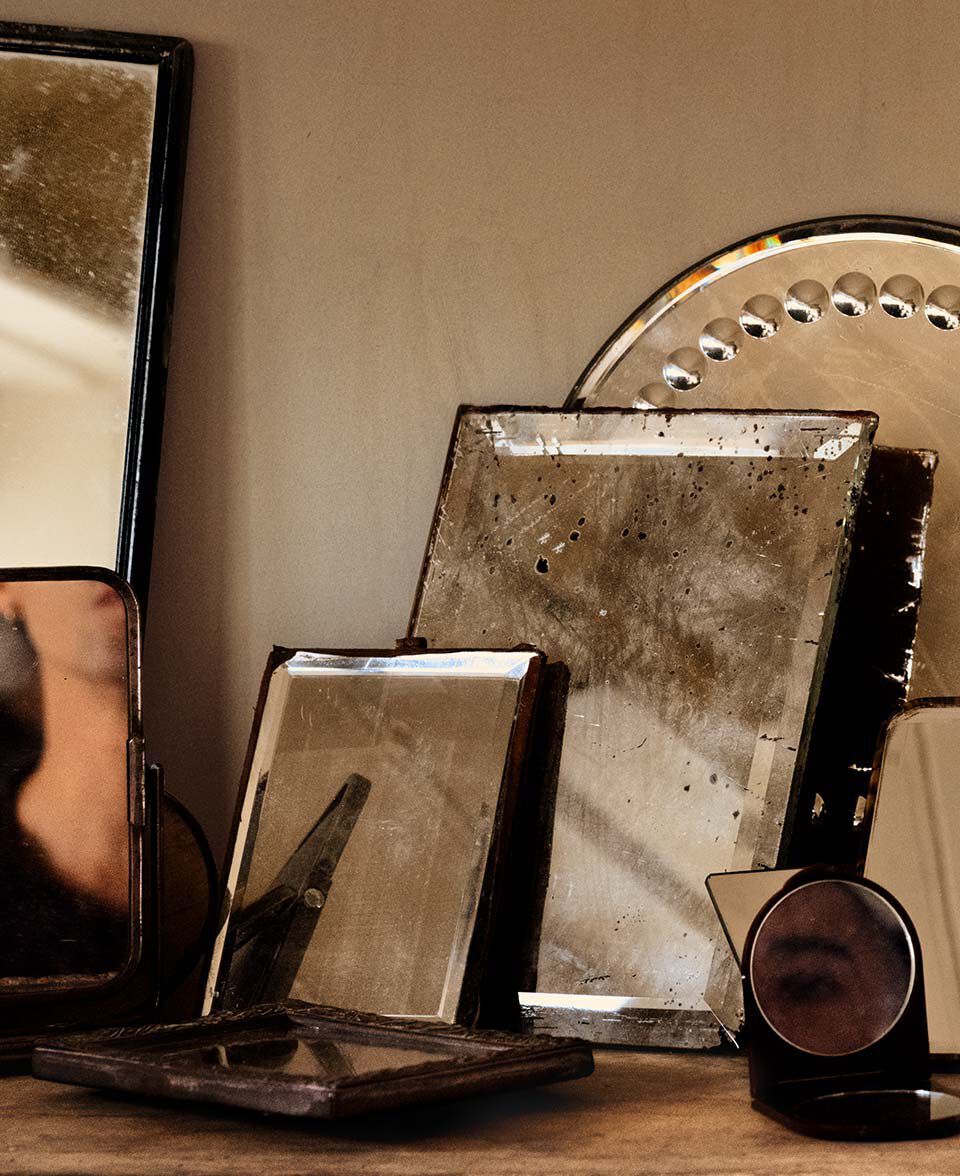 Anordnung antiker Spiegel und reflektierender Objekte auf einer holzernen Tischplatte.